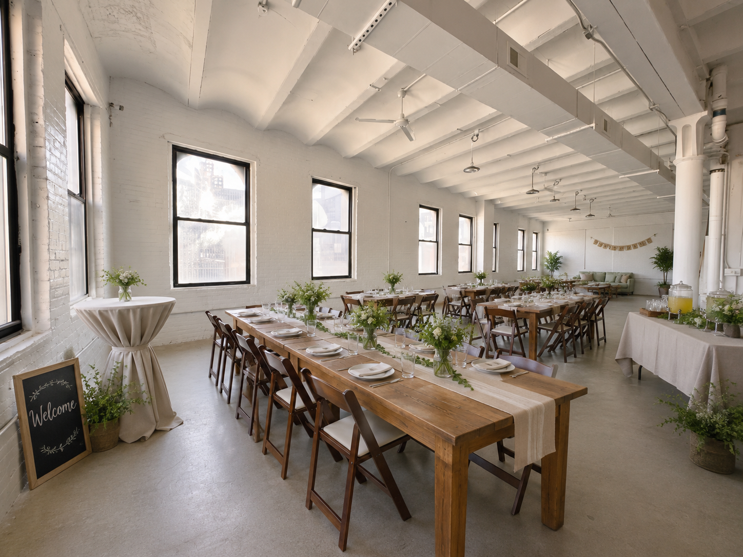 Long farm tables set for a private dinner at EastWick Studio, with a welcome sign and lounge seating in the background