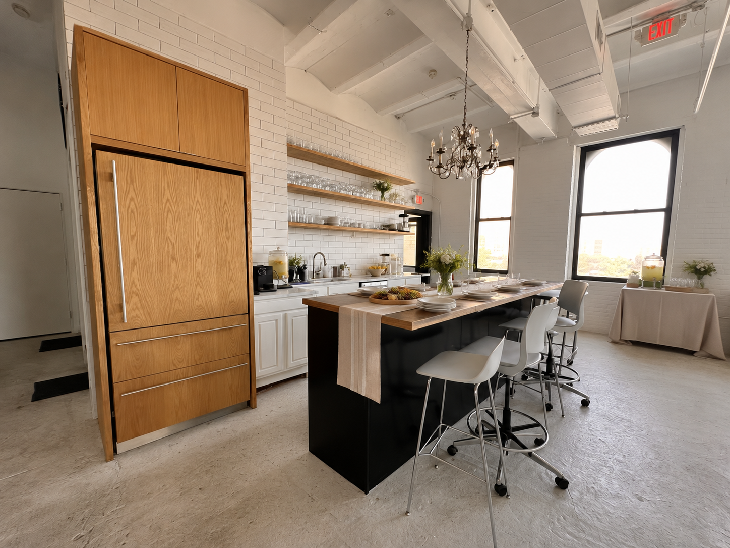 The shared kitchenette set up for catering, with glassware, a chandelier and bar stools at the island